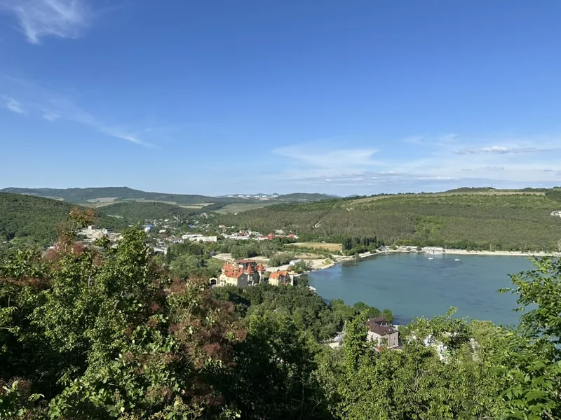Абрау-Дюрсо: панорама озера с высоты — на переднем плане здание с красной черепичной крышей, похожее на замок, дальше бухта с лодками и посёлок на склонах холмов.