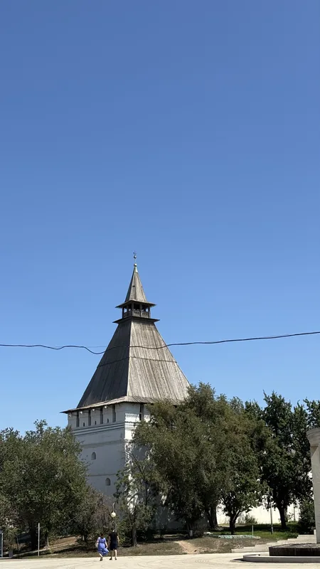 Астраханский кремль: башня с шатровой кровлей среди деревьев, у подножия по дорожке идут люди.