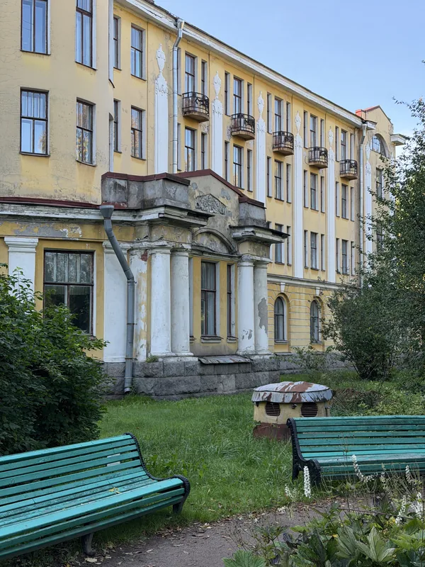 Жёлтое историческое здание с портиком и балконами, перед ним зелёные скамейки