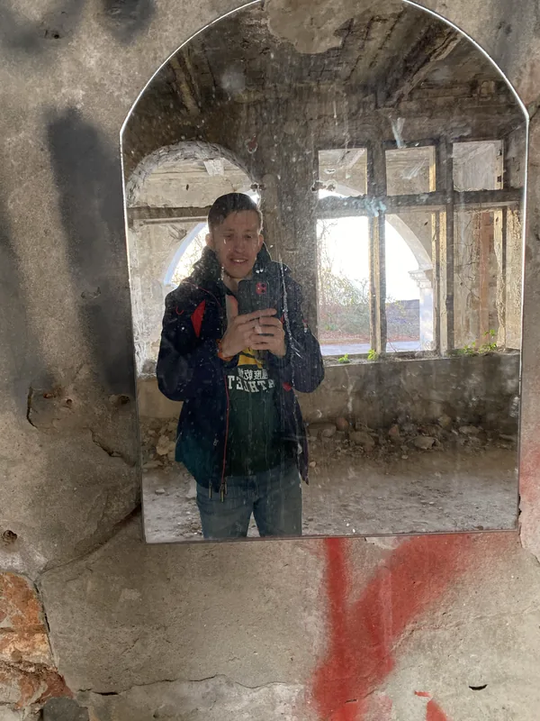 Дача полковника Квитко: посетитель фотографируется в старом настенном зеркале разрушенного зала — за спиной видны арочные окна и осыпающаяся штукатурка.