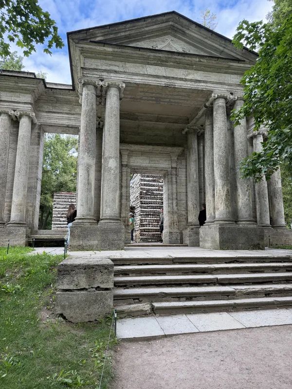 Каменный портик с колоннами и ступенями на поляне парка