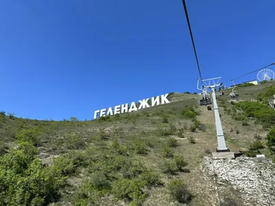 Геленджик: надпись «ГЕЛЕНДЖИК» на склоне хребта у канатной дороги парка «Олимп», вдали видно колесо обозрения.