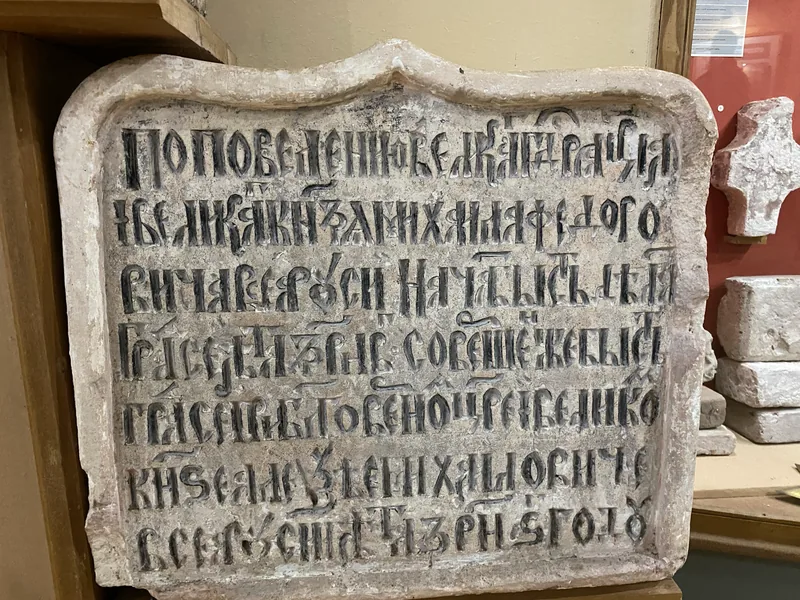 Белокаменная плита с резной надписью старинными кириллическими буквами в музейной витрине