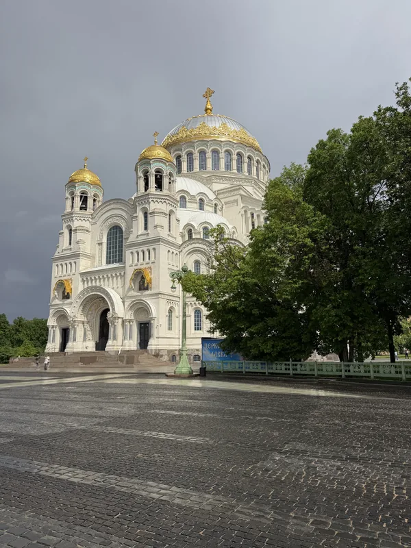 Морской Никольский собор в Кронштадте с Якорной площади перед грозой: тёмное небо, мокрая брусчатка, золотые купола и звонница