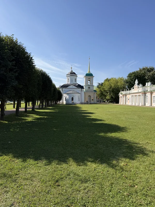 Белая церковь с колокольней в конце аллеи стриженых деревьев