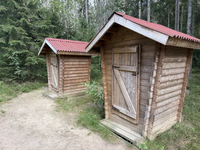 Две деревянные туалетные кабинки под красной крышей рядом с тропой