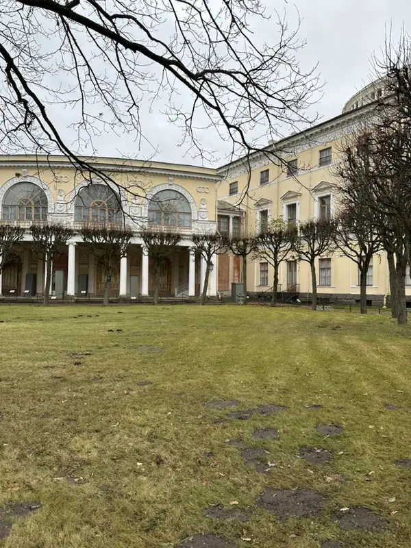 Внутренний двор Павловского дворца: полукруглая галерея с белыми колоннами и лепными арками, жёлтые корпуса и газон с голыми деревьями