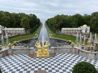 Вид сверху на Большой каскад Петергофа: золочёные скульптуры, круглый ковш фонтана и морской канал, уходящий к заливу