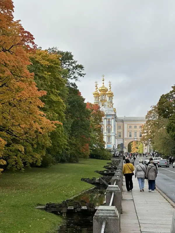 Осенняя аллея вдоль ограды парка, впереди золотые купола дворцовой церкви Екатерининского дворца, по тротуару идут прохожие