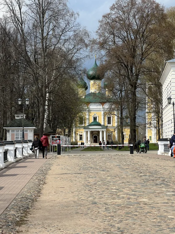 Широкая мощёная дорожка ведёт к жёлто-белому собору с зелёными куполами, по сторонам белая балюстрада, фонари и деревья без листвы