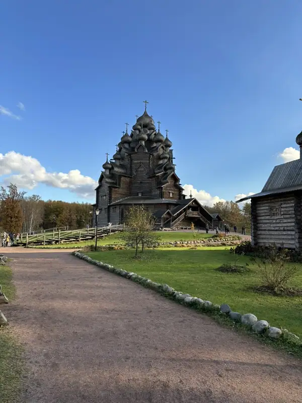Многоглавая деревянная церковь в конце дорожки парка, рядом бревенчатая постройка