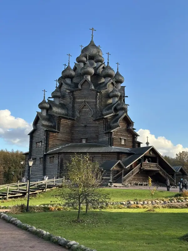 Деревянная Покровская церковь с ярусами глав, покрытых лемехом, на фоне синего неба