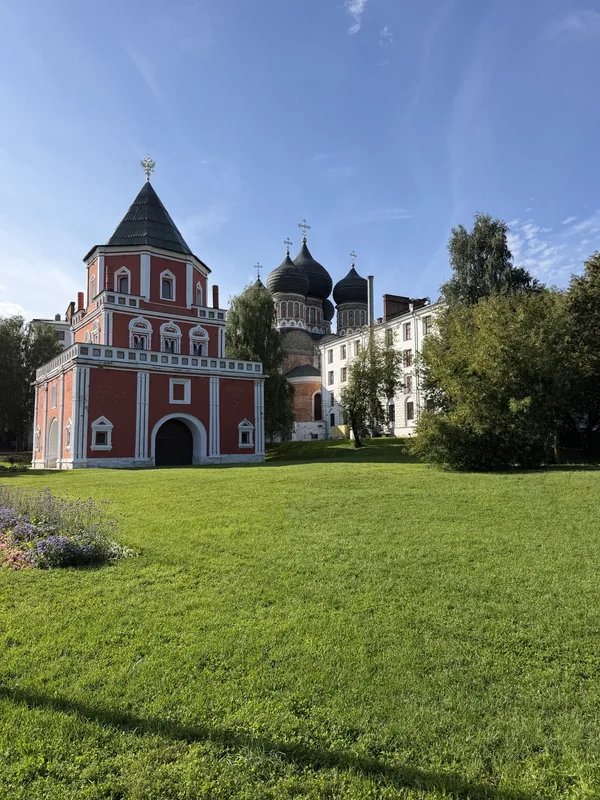 Мостовая башня из красного кирпича и купола Покровского собора за зелёным лугом