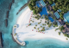 Aerial view of a tropical beach resort with white sand, turquoise water, palm trees, and blue-roofed buildings along the shore.
