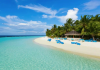Turquoise lagoon with white sandy beach, palm trees, and blue lounge chairs by a thatched hut under a clear blue sky.