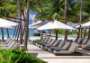 Row of poolside lounge chairs under white umbrellas along a palm-lined beach with turquoise water in the background